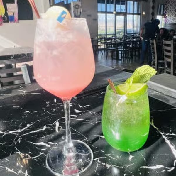 Two colorful cocktails, one pink and one green, on a black marble table in a restaurant.