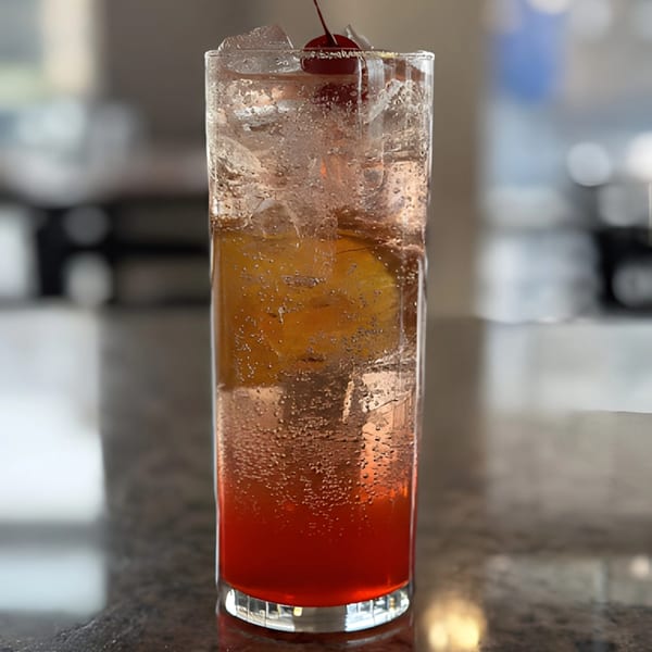 Tall glass of a bubbly red and orange drink with ice and a cherry on top.