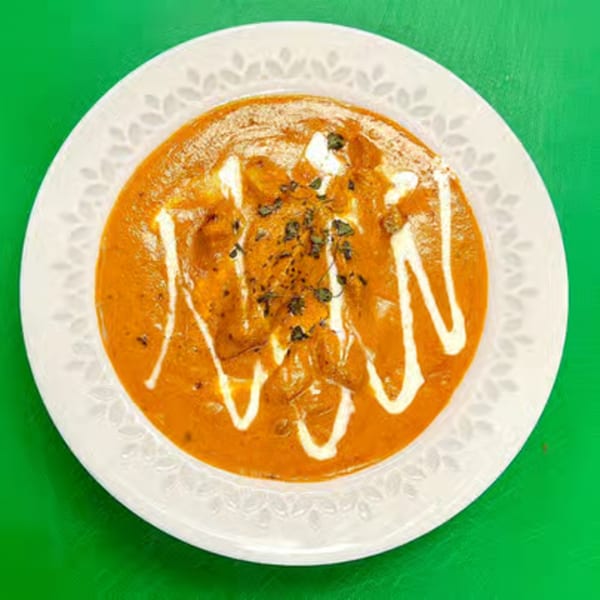 A white plate filled with orange curry, drizzled with white cream and garnished with herbs.