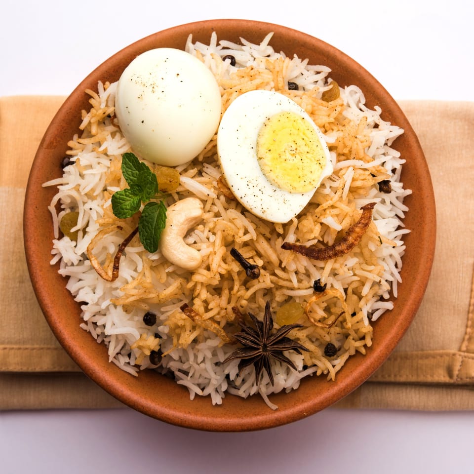 Egg Biryani in a terracotta bowl, garnished with mint, cashews, and spices.